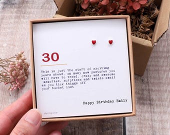 May include: A small, white card with the number 30 printed in red. The card has a message that reads "This is just the start of exciting years ahead, on many new pastures you will have to tread. Crazy and awesome memories, surprises and twists await as you tick things off your bucket list." The card also has the text "Happy Birthday Emily" and "sterling silver". There are two small red hearts at the top of the card.