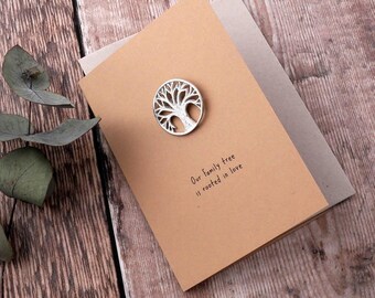 May include: A brown card with the text "Our family tree is rooted in love" and a silver tree cutout attached to the card.