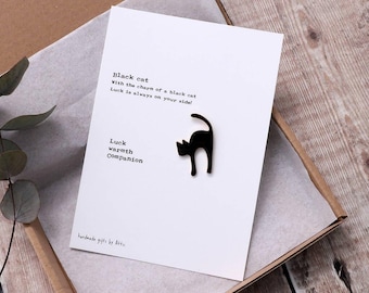 May include: A white card with the text "Black cat" and a black cat silhouette. The card also includes the phrases "Luck, warmth, Companion" and "Luck is always on your side!" The card is inside a brown box.