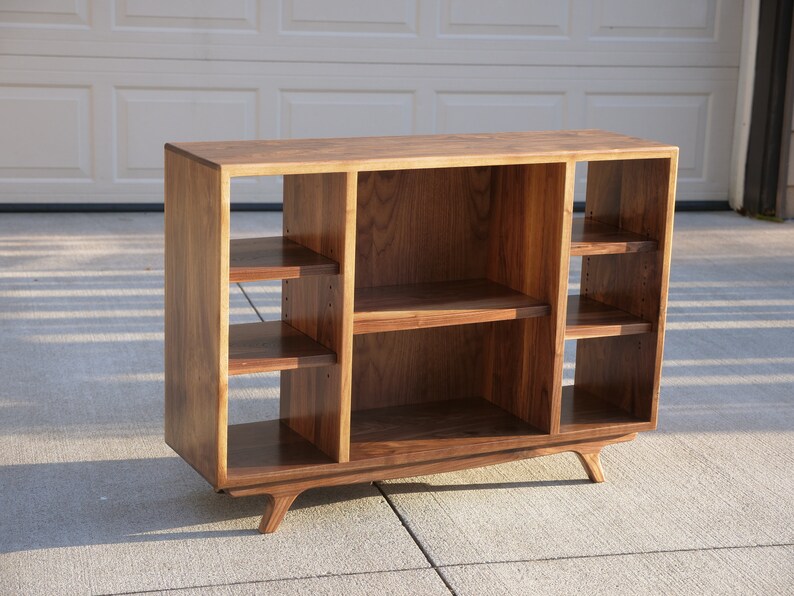 May include: A wooden entertainment center with a mid-century modern design. It has a dark walnut finish and features multiple shelves for displaying items. The unit has four legs that are angled outward.