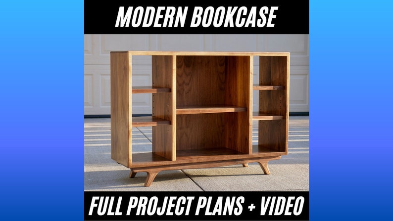 May include: A modern bookcase made of wood with a light brown finish. The bookcase has three shelves on each side and a larger shelf in the middle. The bookcase has a simple design with rounded legs.