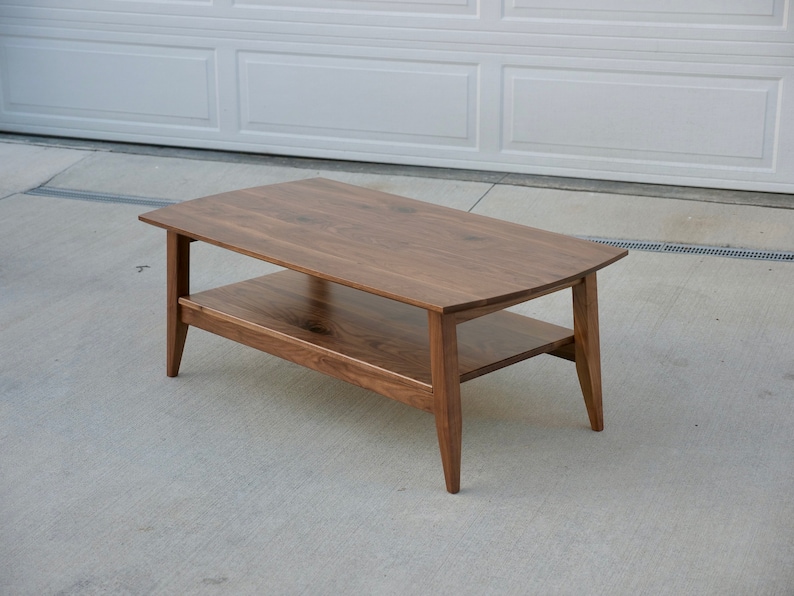 May include: A rectangular coffee table made of dark brown wood. The table has a lower shelf and angled legs. The table is approximately 48 inches long, 24 inches wide, and 18 inches high.