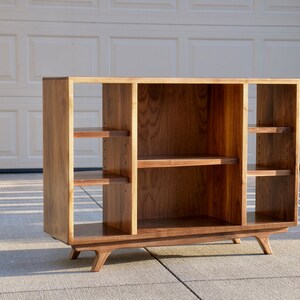 May include: A wooden entertainment center with four open shelves and a lower shelf. The entertainment center has a mid-century modern design with angled legs.