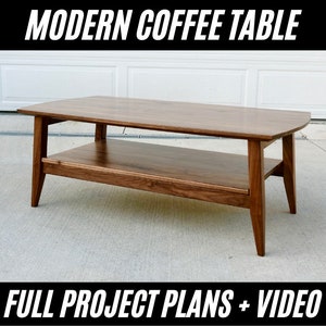 Puede incluir: Mesa de centro moderna de madera con estante inferior. La mesa tiene una tapa rectangular con esquinas redondeadas y patas anguladas. Se muestra el texto "MODERN COFFEE TABLE" y "FULL PROJECT PLANS + VIDEO".