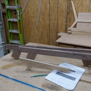 May include: A wooden workbench with a piece of wood on top. The wood is shaped like a gun and has a green pencil next to it. There is a piece of paper with a drawing on it.