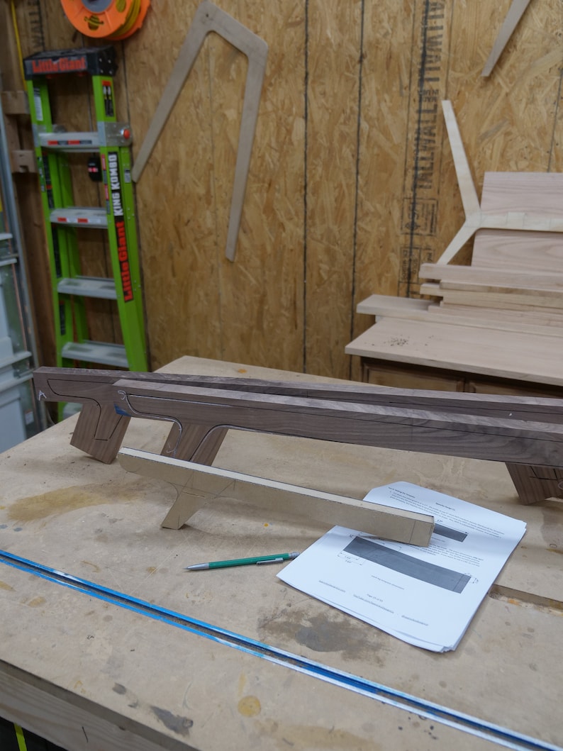 May include: A wooden workbench with a piece of wood on top. The wood is shaped like a gun and has a green pencil next to it. There is a piece of paper with a drawing on it.