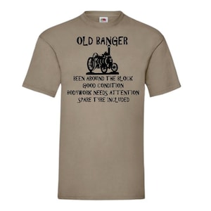 May include: A khaki t-shirt with a black graphic of a vintage steam engine. The text on the shirt reads "Old Banger, Been around the block, Good condition, Bodywork needs attention, Spare tyre included."