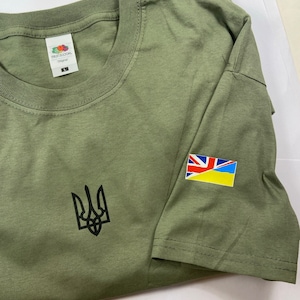 May include: A green t-shirt with a black Ukrainian trident symbol on the front and a yellow and blue Ukrainian flag with a Union Jack patch on the right sleeve. The t-shirt is made by Fruit of the Loom.