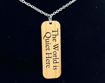May include: A wooden pendant necklace with a silver chain. The pendant is rectangular and has the text "The World is Quiet Here" engraved on it.