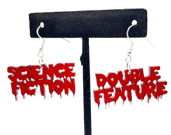 Puede incluir: Un par de pendientes rojos colgantes con las palabras "Science Fiction" y "Double Feature" en una fuente que gotea.