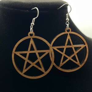 May include: A pair of wooden earrings with a pentagon star design. The earrings are brown and have silver hooks.