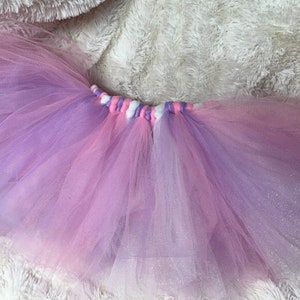 Può includere: Un tutù di tulle rosa e viola con una cintura intrecciata bianca e rosa.