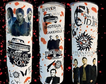 May include: Three white stainless steel tumblers with a red splatter paint design. The tumblers feature images and text from the TV show Supernatural. The text includes "Driver picks the music", "Shotgun shuts his cakehole", "Carry on my wayward son", "Winchester Supernatural", "Don't be an idjit", and "Supernatural join the hunt".