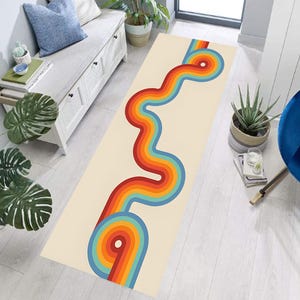 May include: A rectangular rug with a retro design. The rug features a cream-colored background with a wavy, colorful pattern in shades of red, orange, yellow, blue, and green. The design resembles a stylized road or river.
