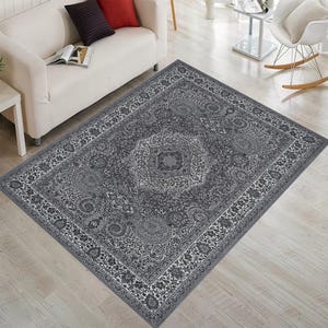 Puede incluir: Una alfombra de área gris y blanca con un diseño tradicional. La alfombra tiene un medallón central y un borde con detalles intrincados.