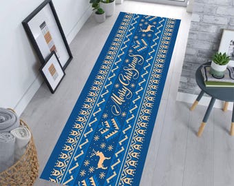 Op de afbeelding: Een blauwe kerstlopermat met een feestelijk ontwerp. Het tapijt heeft een herhalend patroon van sneeuwvlokken, rendieren en geometrische vormen in crème en goud. De woorden "Merry Christmas" zijn in cursiefschrift in het midden geschreven.