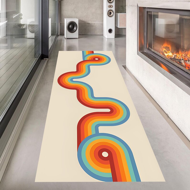 May include: A rectangular rug with a cream background and a retro-style design. The design features a wavy, colorful pattern in shades of red, orange, yellow, blue, and green. The rug is placed on a polished concrete floor.