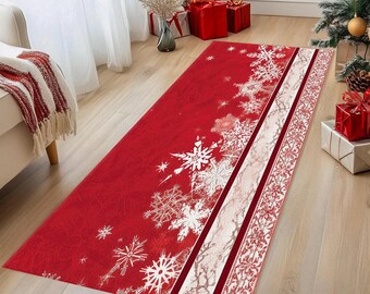 Op de afbeelding: Een rode rechthoekige vloerkleed met een sneeuwvlokontwerp. Het vloerkleed heeft grote witte sneeuwvlokken en een wit en rood gestreepte rand. Het vloerkleed ligt op een houten vloer, met een kerstboom en cadeaus op de achtergrond.