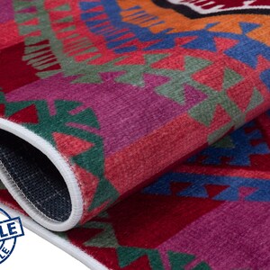 May include: Close-up of a colorful rug with geometric patterns in shades of red, orange, blue, green, and purple. The rug has a white border and is folded in half.