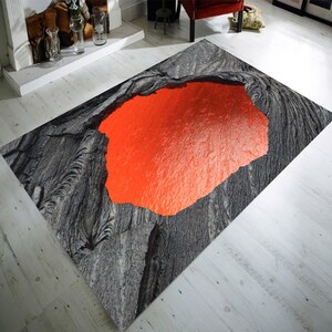 May include: A black and grey area rug with a large, bright orange, circular opening that resembles a volcano. The opening is filled with a bright orange, lava-like substance.