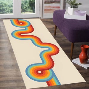 May include: A rectangular rug with a cream-colored background features a vibrant, retro-style design. A wavy, rainbow-colored pattern in shades of red, orange, yellow, green, and blue runs along the length of the rug, creating a bold visual statement.