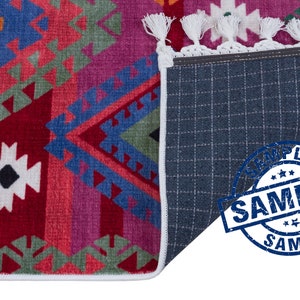 May include: A colorful rug with a geometric pattern in shades of red, blue, green, and orange. The rug has a white fringe border and a gray backing. The word "SAMPLE" is stamped in blue on the backing.