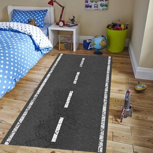May include: A grey and white road rug with white lines down the centre. The rug is laid out on a wooden floor in a room with a bed and a bedside table.