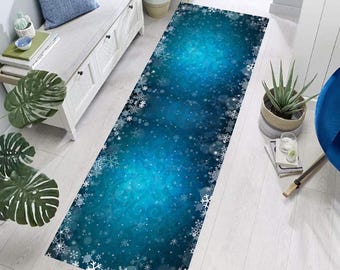Op de afbeelding: Een rechthoekig vloerkleed met een blauwe gradiënt achtergrond en een sneeuwvlokkenrand. Het vloerkleed heeft een winterthema, met witte sneeuwvlokken verspreid over het oppervlak. Het vloerkleed is ontworpen voor gebruik binnenshuis.