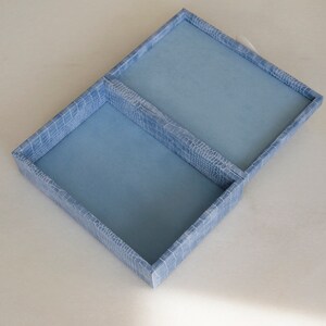 May include: A light blue jewellery box with two compartments. The box has a textured, crocodile-embossed design.