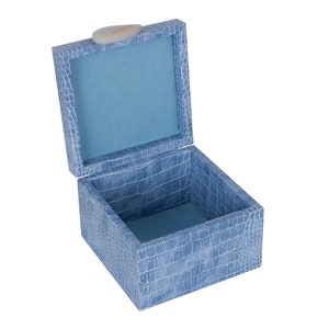 May include: A light blue decorative box with a crocodile-embossed pattern and a white shell-shaped knob on the lid. The box is open and the inside is lined with a light blue fabric.