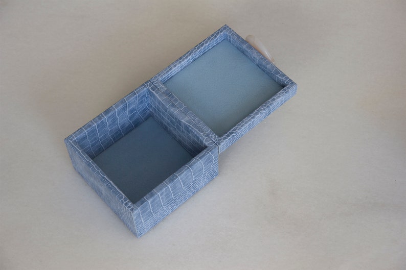 May include: A light blue, two-compartment box with a crocodile-embossed pattern. The box is open, revealing a blue interior.