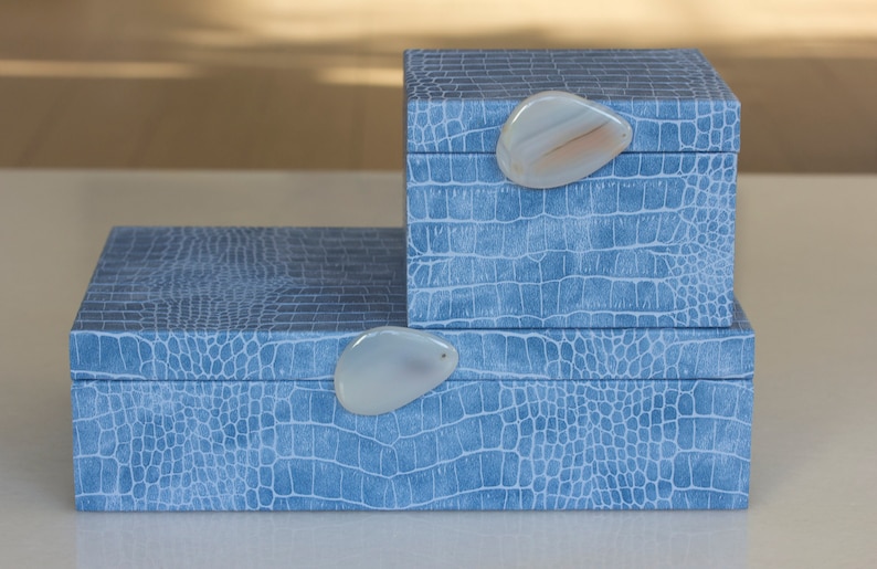 May include: Two blue boxes with a crocodile skin pattern. The boxes have agate stone handles. The smaller box is stacked on top of the larger box.