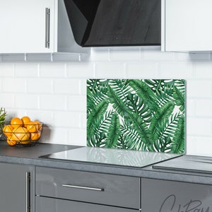 May include: A green and white kitchen backsplash with a tropical leaf design. The backsplash is installed behind a glass top stove.