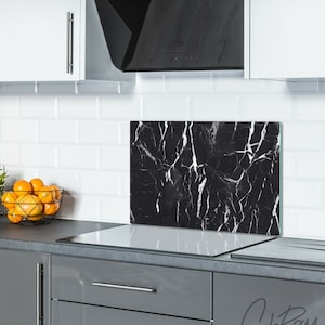 May include: Black and white marble patterned glass kitchen backsplash with a white countertop and gray cabinets. The backsplash is installed above a white electric stovetop.
