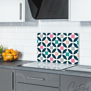 May include: A white, gray, teal, and pink geometric patterned kitchen backsplash with a white background. The backsplash is installed above a black electric stovetop.