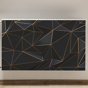 Op de afbeelding: Een zwarte radiator met een gouden geometrisch patroon. De radiator is gemonteerd aan een witte muur.