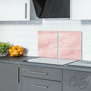 Peut inclure: Deux protections de cuisinière en verre à motif marbré rose, chacune mesurant environ 30 cm sur 30 cm, sont placées sur un plan de travail gris dans une cuisine. Les protections sont conçues pour empêcher les dommages causés par la chaleur au plan de travail.