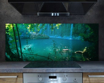 Puede incluir: Una campana extractora negra con un protector contra salpicaduras con una escena de cascada. El protector contra salpicaduras presenta una exuberante jungla verde con una cascada que fluye hacia una piscina turquesa.