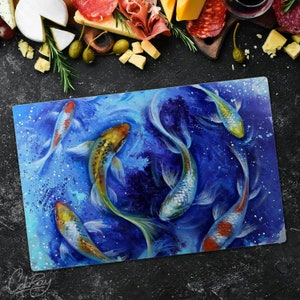Puede incluir: Una tabla de cortar de vidrio azul con una pintura de acuarela de cinco peces koi coloridos nadando en un estanque azul. Los peces están pintados en tonos de naranja, amarillo, blanco y negro.