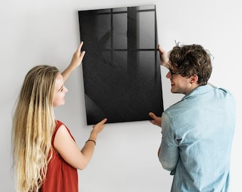 Puede incluir: Dos personas están colgando un cuadro negro enmarcado en una pared blanca. El cuadro es un diseño abstracto en blanco y negro.