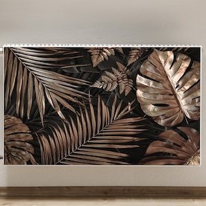 May include: A white radiator cover featuring a tropical leaf design. The leaves are gold and black and are arranged in a random pattern.