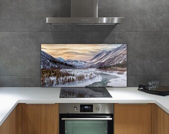 Puede incluir: Un protector de salpicaduras de cocina con una imagen panorámica de una cordillera nevada y un río serpenteando por el valle. El protector de salpicaduras está instalado detrás de una estufa y un horno de acero inoxidable.