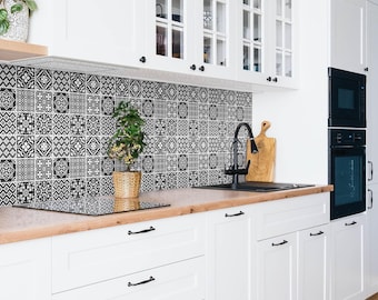 May include: A kitchen featuring white cabinets with black hardware, a light wood countertop, and a backsplash composed of square black and white patterned tiles. A black faucet is positioned over a sink, with a small potted plant nearby.