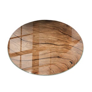 May include: Oval glass chopping board featuring a wood grain pattern. The glass surface reflects light, highlighting the natural wood texture. The board is light brown and has a smooth, polished finish.