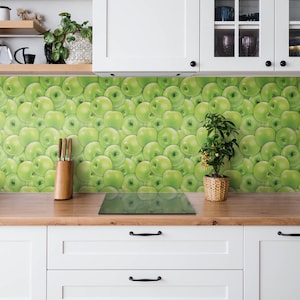 Puede incluir: Una cocina blanca con papel tapiz de manzanas verdes, una encimera de madera y armarios blancos con tiradores negros. Hay una placa de cocción eléctrica negra y una pequeña planta en maceta en la encimera.