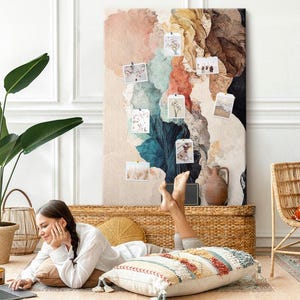 May include: A large rectangular canvas wall art piece featuring an abstract watercolour design in shades of peach, teal, deep blue, brown, and cream. Several small rectangular photographs are pinned to the surface of the canvas.