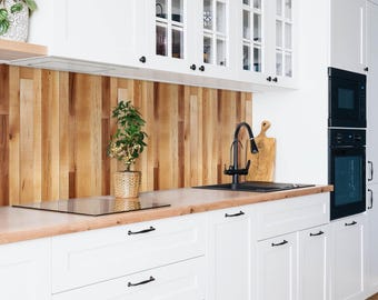 May include: A kitchen featuring white shaker cabinets with black hardware, a light wood countertop, and a vertical wood plank backsplash. A black faucet is mounted over a black sink, with a small potted plant and a wooden cutting board nearby.