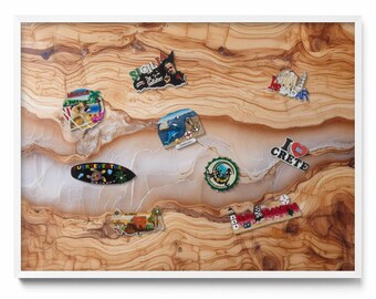 May include: A collection of travel souvenir magnets on a wooden surface. The magnets feature various designs, including landscapes, text, and illustrations. The wooden surface has a natural grain pattern and is framed in white.