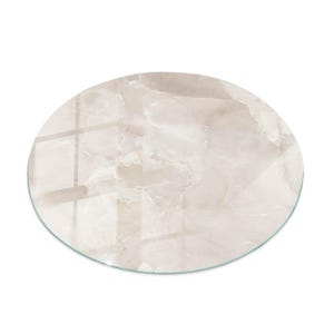Peut inclure: Une table ronde en verre avec un motif marbré. La surface présente un mélange de tons beige et crème avec de fines veines, imitant la pierre naturelle. Le bord de la table est transparent.