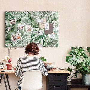 May include: A rectangular wall-mounted notice board featuring a vibrant green tropical palm leaf pattern. The board is covered with various small photographs, white note cards, and a card with the handwritten text Thank you pinned to the surface.